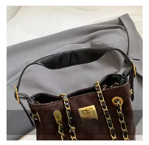 Detail of brown quilted suede handbag featuring a gold square lock and chain strap