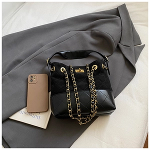 Detail of a black quilted leather bucket bag with gold chain strap on grey fabric
