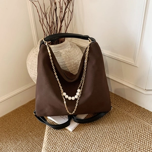 Brown suede shoulder bag with gold chain and pearls on a textured background