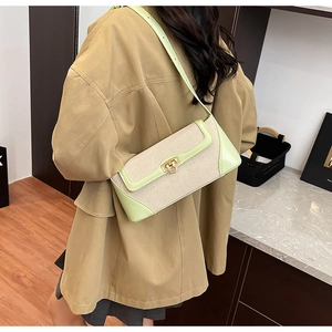 Green and beige patchwork baguette bag with canvas texture and gold metal buckle worn by model