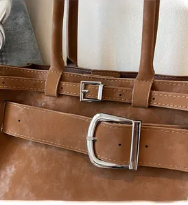 Detail of brown suede shoulder bag with dual silver square metal buckles on the front