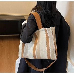 Detailed side view of large striped canvas tote bag with brown woven straps for daily commuting
