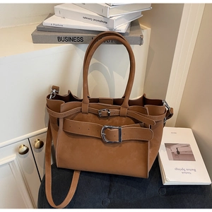 Detail of a brown suede tote bag featuring a large silver metal buckle and adjustable strap