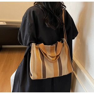 Detail of striped canvas tote bag with wide straps shown on a shoulder in warm light