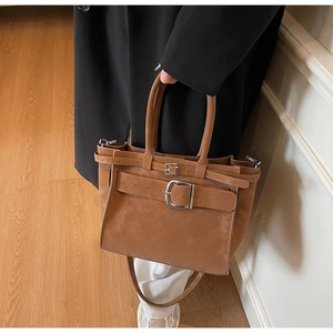 Detail of brown suede tote bag with decorative buckle straps and silver hardware