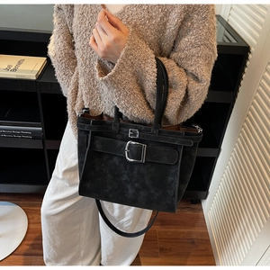 Detail of black suede tote bag with silver buckle worn with a beige sweater