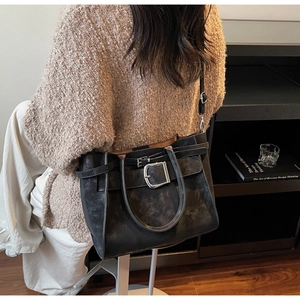 Detail of black matte suede shoulder bag with decorative buckle straps and top handles