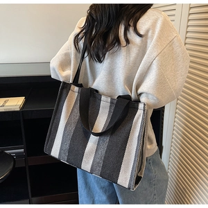 Detailed view of large striped canvas tote bag worn by a model in a minimalist setting