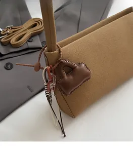 Detail of brown canvas baguette bag with leather charm and yellow smiley face pendant
