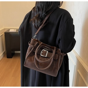 Detail of coffee brown suede shoulder bag with silver buckle on the back of a model