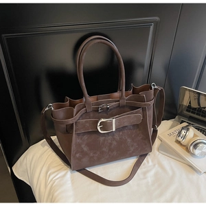 Macro detail of brown suede tote bag featuring silver buckle and smooth zipper closure