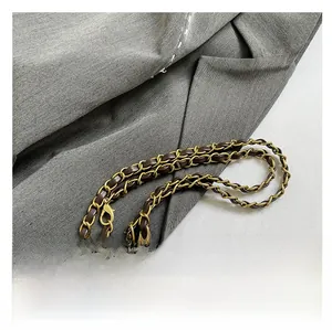 Detail of gold metal chain woven with dark brown leather strap and lobster clasp