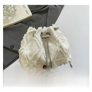 Detail of white denim bucket bag with fringe texture and thick silver chain strap
