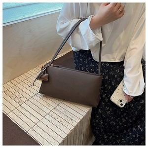 Detail of dark brown leather underarm bag featuring heart charm and striped scarf accent