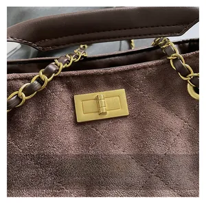 Detail of dark brown quilted suede texture with gold metal twist lock and chain strap