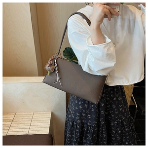 Brown underarm bag with woven tassel detail on textured leather in a lifestyle setting
