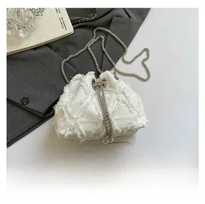 Macro shot of denim bucket bag with frayed edges, pearl charms, and smartphone size comparison
