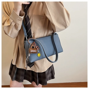 Detail of dark blue-grey shoulder bag with yellow smiley face and brown charms