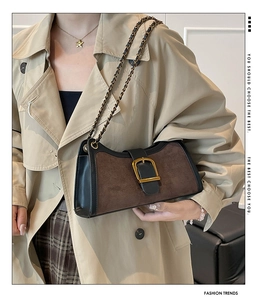 Detail of dark brown baguette bag with gold buckle and chain on trench coat
