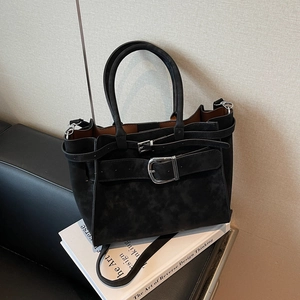 Detail view of black faux suede handbag with decorative buckles on vintage books