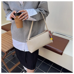 Close-up of beige minimalist baguette shoulder bag with yellow smiley face charm pendant