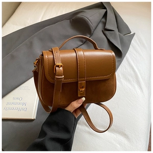 Detail of caramel leather crossbody bag featuring gold twist lock and mixed textures