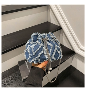 Close-up of denim bucket bag showing floral texture, silver chain and pearl drawstring
