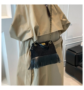 Detail of black quilted leather bag with long tassels and gold chain strap on beige coat