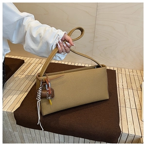 Detail of khaki fabric baguette bag featuring decorative woven cords and trendy side charms