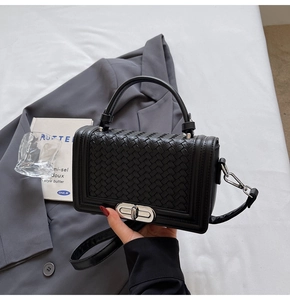 Close-up of black woven leather crossbody bag with silver twist lock and round handle