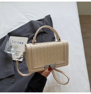 Close-up of beige woven texture with silver twist lock on stylish flap handbag