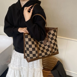 Detail of checkered canvas tote bag with brown leather handles worn by a model