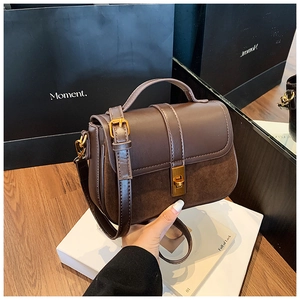 Detail of a brown textured leather crossbody bag with suede panels and gold metal buckle lock