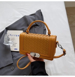 Detail of ginger yellow woven handbag showing silver twist lock and handle texture