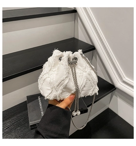 Detail of white denim bucket bag featuring frayed patchwork and pearl drawstring accents