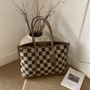 Detailed view of the checkered canvas tote bag with brown leather handles on a textured mat