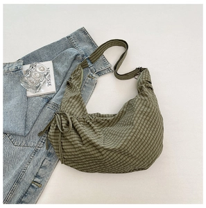 Detail of green gingham dumpling bag featuring drawstring sides and woven strap