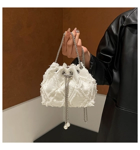 Detail of white canvas bucket bag featuring silver chain drawstring and pearl accents