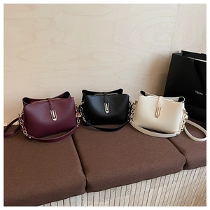 Three leather crossbody bags in burgundy, black, and cream with metal chain details