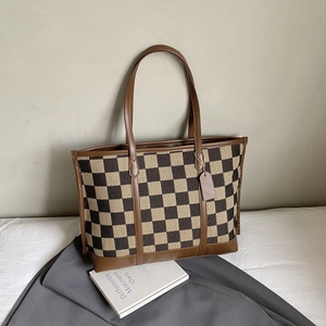 Detail of checkered canvas tote bag with brown leather handles and tag on a soft fabric base