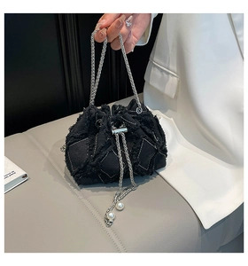 Detail of black denim bucket bag featuring raw edges, chain strap and large pearl charms