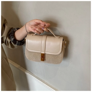 Detail view of beige textured handbag featuring a gold metallic twist lock and handle