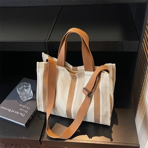 Large striped canvas tote bag with brown straps and detachable shoulder strap on display