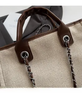 Detail of canvas tote bag showing silver eyelets, brown leather handles and chain strap