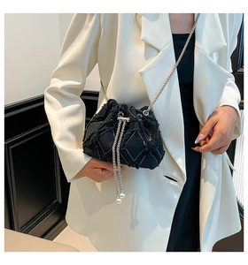 Close-up of denim bucket bag with frayed edges, silver chain, and pearl drawstrings