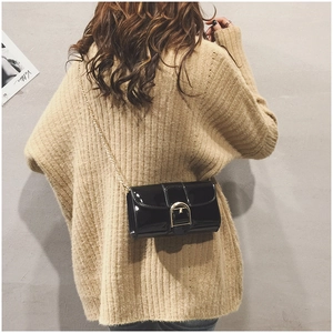 Détail d'un sac bandoulière en cuir verni noir avec chaîne dorée porté par un mannequin