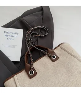 Detail of beige canvas tote with brown leather trim and metal chain shoulder strap