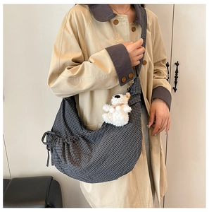 Detail of checkered crossbody crescent bag with drawstring texture and plush puppy charm