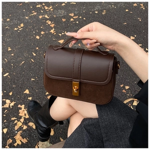 Detail of dark brown crossbody bag with gold twist lock on autumn leaves background