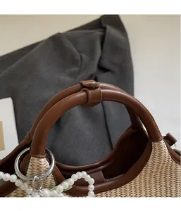 Detail der Strohhandtasche mit braunem Ledergriff und elegantem Perlenanhänger-Detail